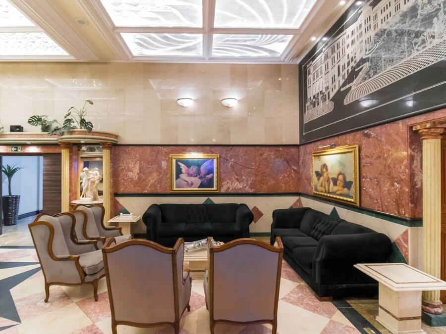 A lobby with a black sofa, beige armchairs, a marble floor, and a large painting on the wall.