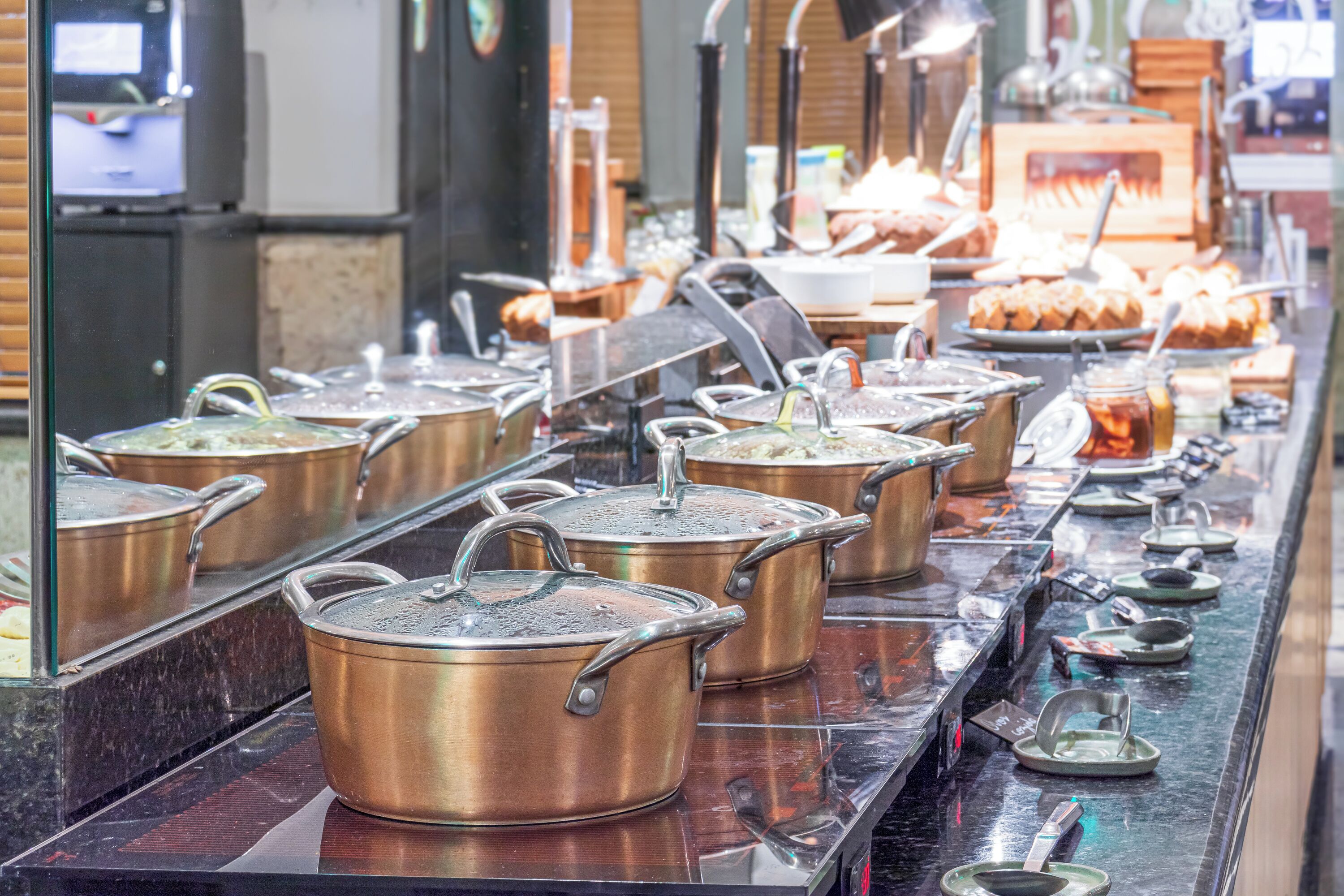 Una linea di buffet con diverse postazioni gastronomiche, tra cui pentole calde e una varietà di piatti.