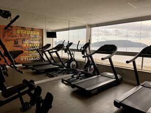 Un gimnasio con cintas de correr y máquinas de pesas, ventanas amplias con vistas a montañas y carteles motivacionales en las paredes.