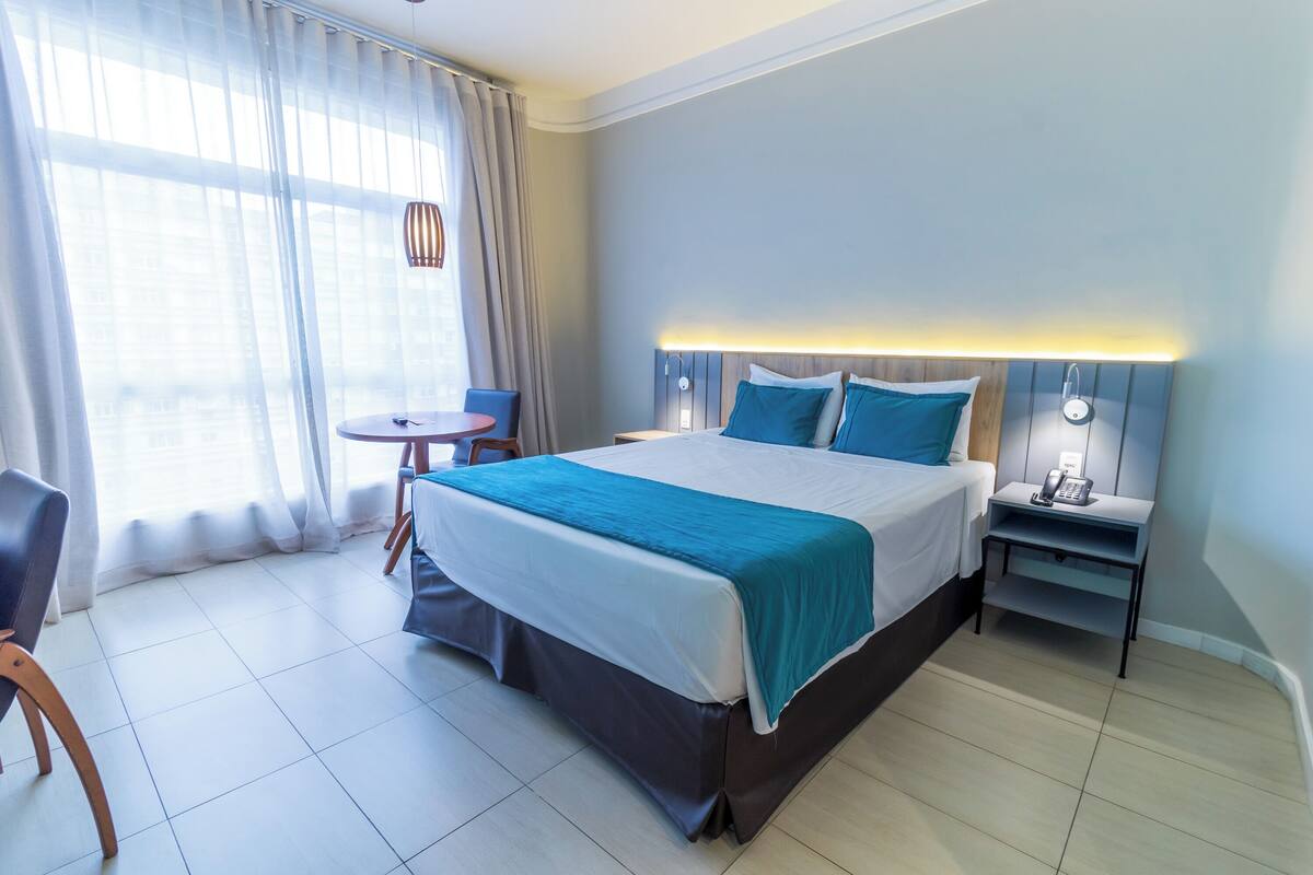 A hotel room with a large bed, bedside tables, a small round table, and a chair.