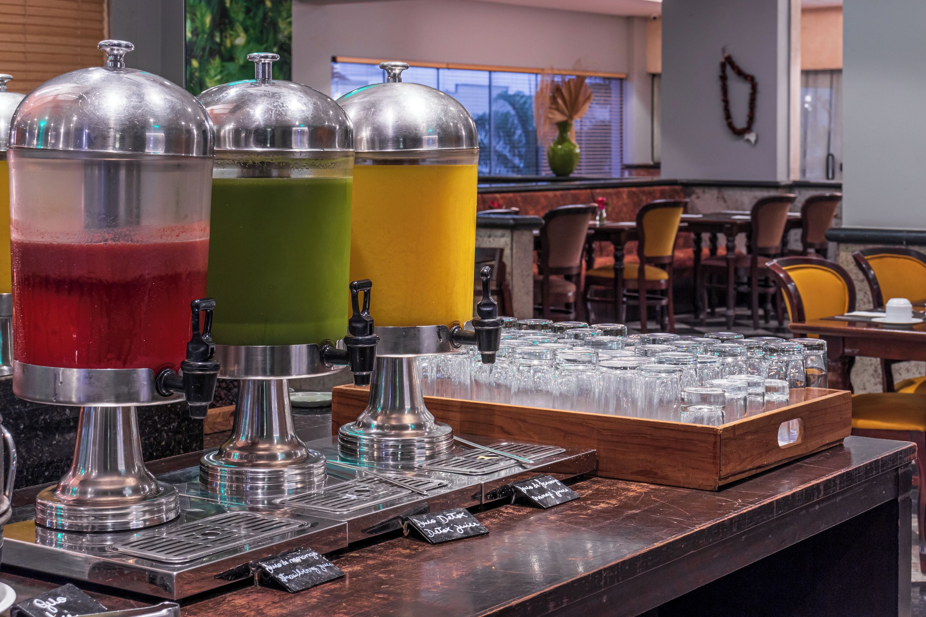 Estación de bebidas con tres dispensadores llenos de bebidas de diferentes colores, una bandeja de vasos y una máquina de café.