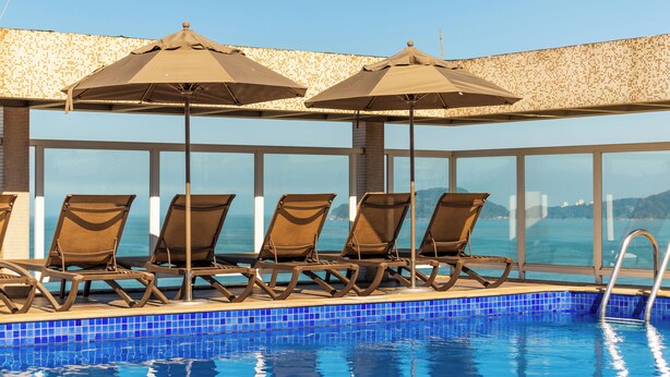 A poolside area with lounge chairs and umbrellas, a clear view of the sea, and a tiled pool. - Parque Balneário Hotel Santos by Castelo Itaipava (Santos)