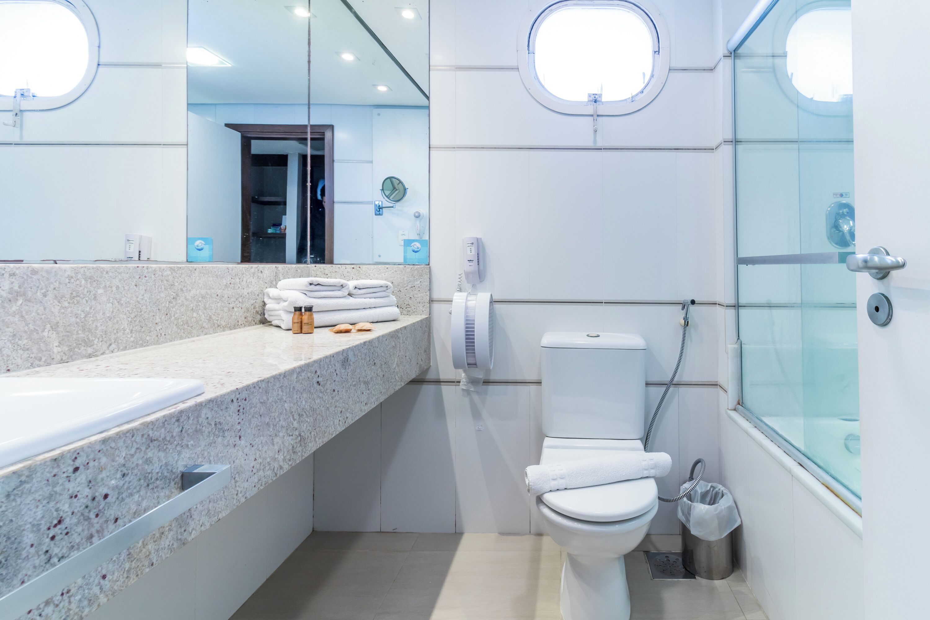 A modern bathroom with a granite countertop, a toilet, a glass-enclosed shower, and a large mirror.