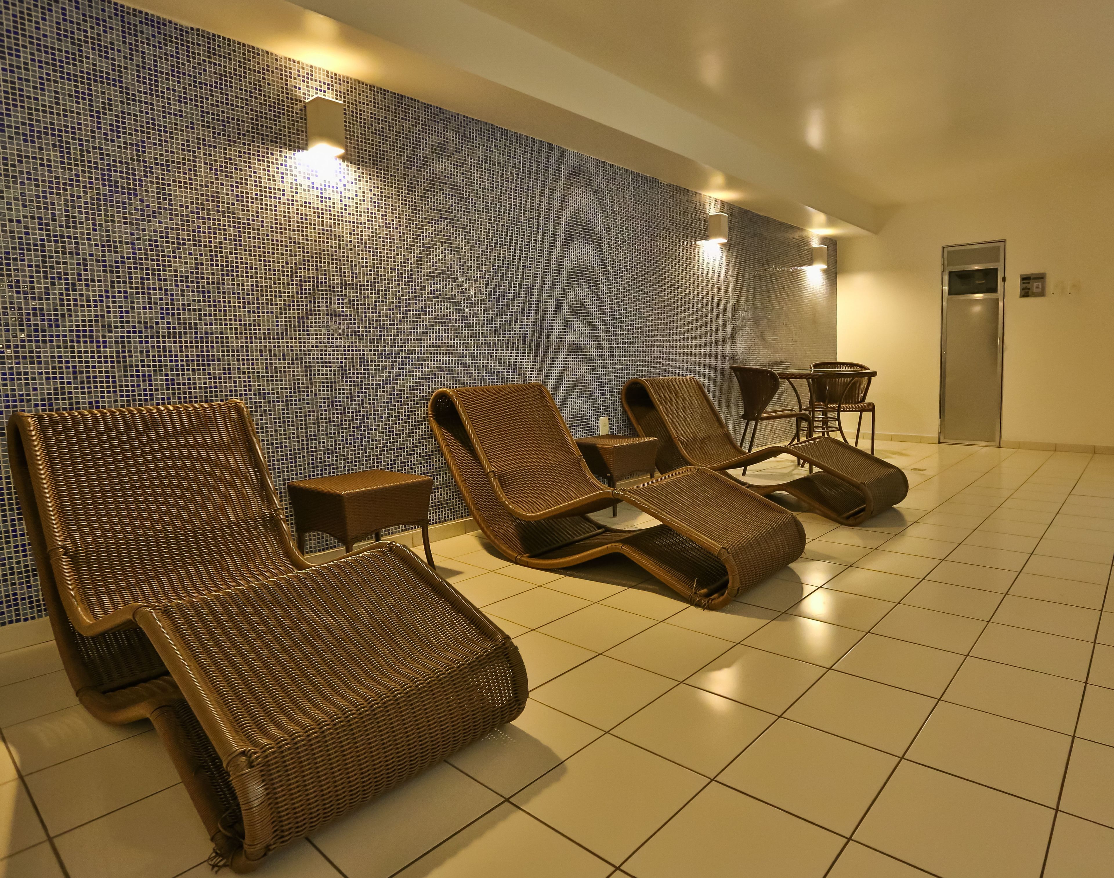 A room with four wicker lounge chairs, a small table, and a wall with a mosaic tile pattern.