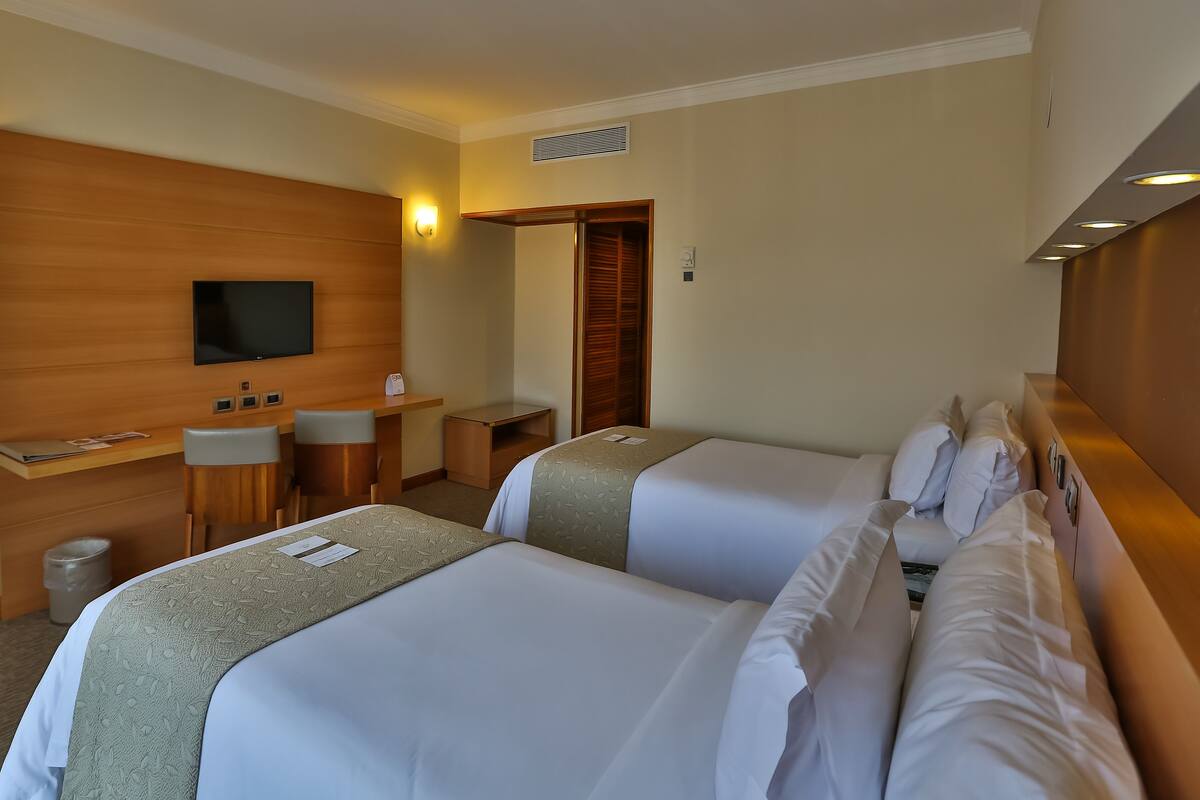 Ein Hotelzimmer mit zwei Betten, einem Schreibtisch, einem Sessel, einem Fernseher und einem Holzschrank.