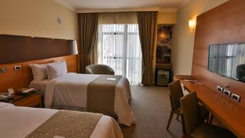 A hotel room with two beds, a desk, a chair, a television, and a window with curtains.