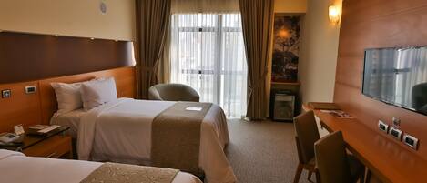 A hotel room with two beds, a desk, a chair, a television, and a window with curtains.