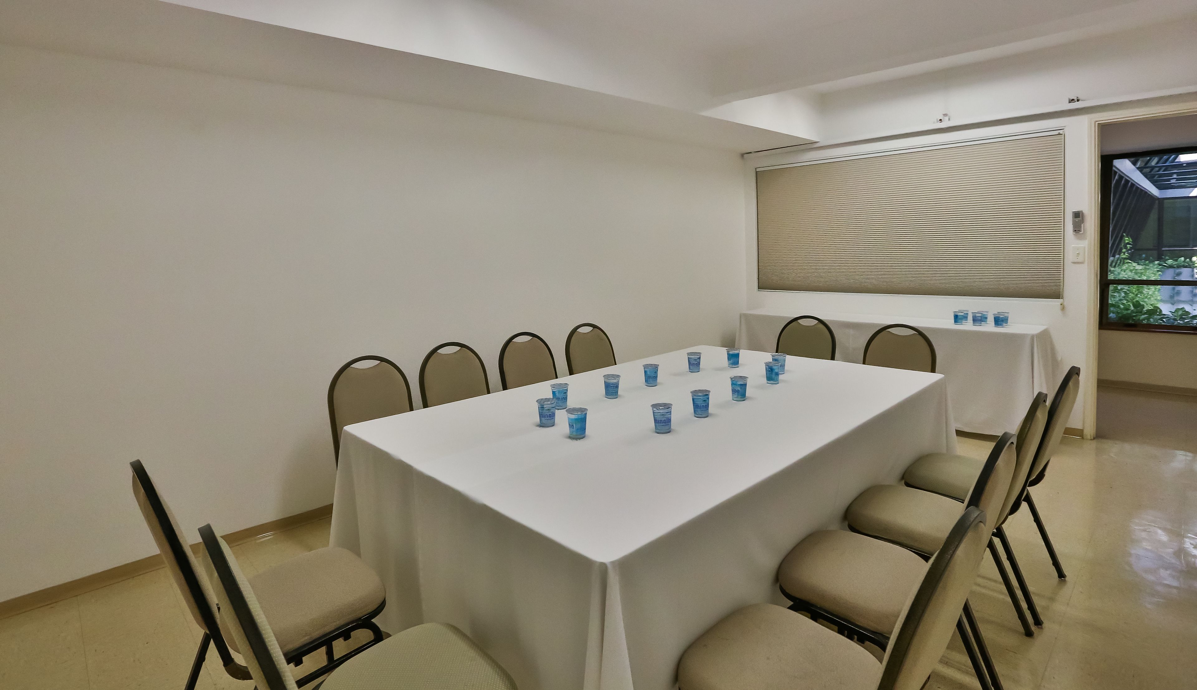 A conference room with a white table, beige chairs, and blue water bottles on the table.