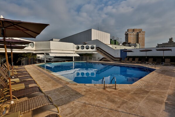 Una piscina en la azotea con sillones de descanso y sombrillas, rodeada de edificios modernos.