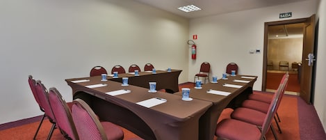 A conference room with a long table, red chairs, and a fire extinguisher on the wall.