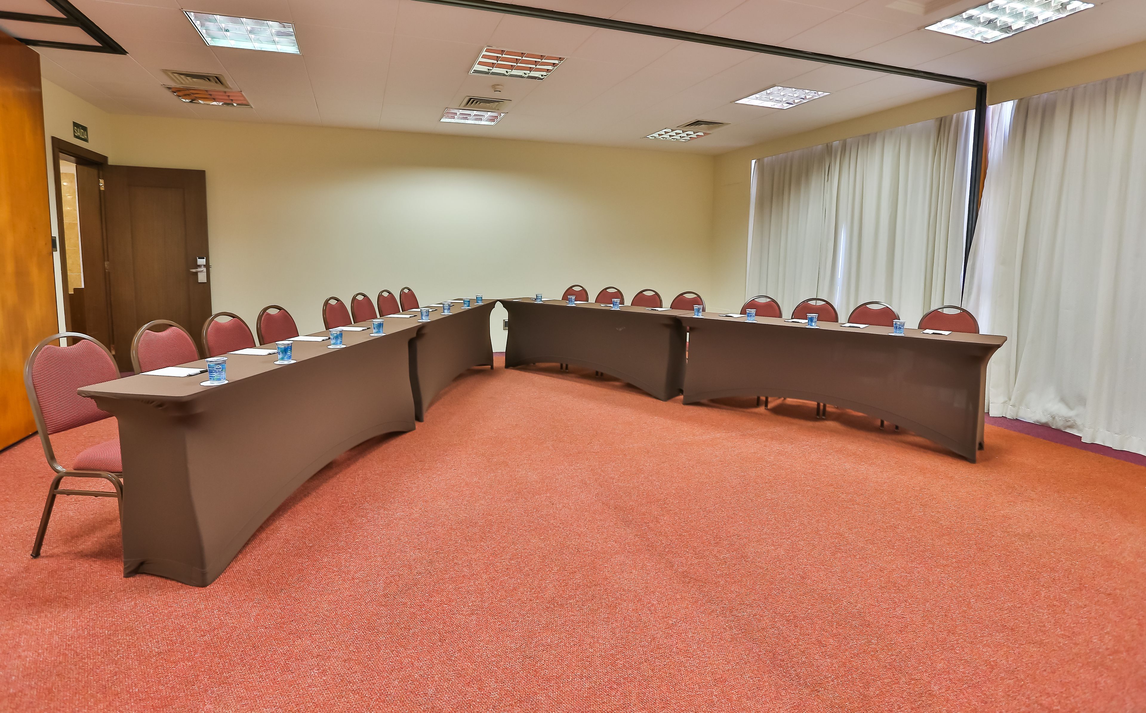 Un salón de conferencias con una larga mesa, sillas rojas y suelo alfombrado.