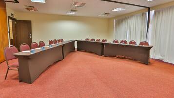 Un salón de conferencias con una larga mesa, sillas rojas y suelo alfombrado.