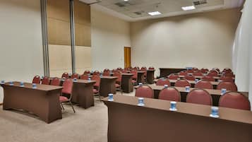 Un salón de conferencias con filas de mesas y sillas, equipado con botellas de agua.