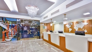 Un moderno vestíbulo de hotel con suelo de mármol, mostrador de recepción, un mural de un mapa mundial y una araña.