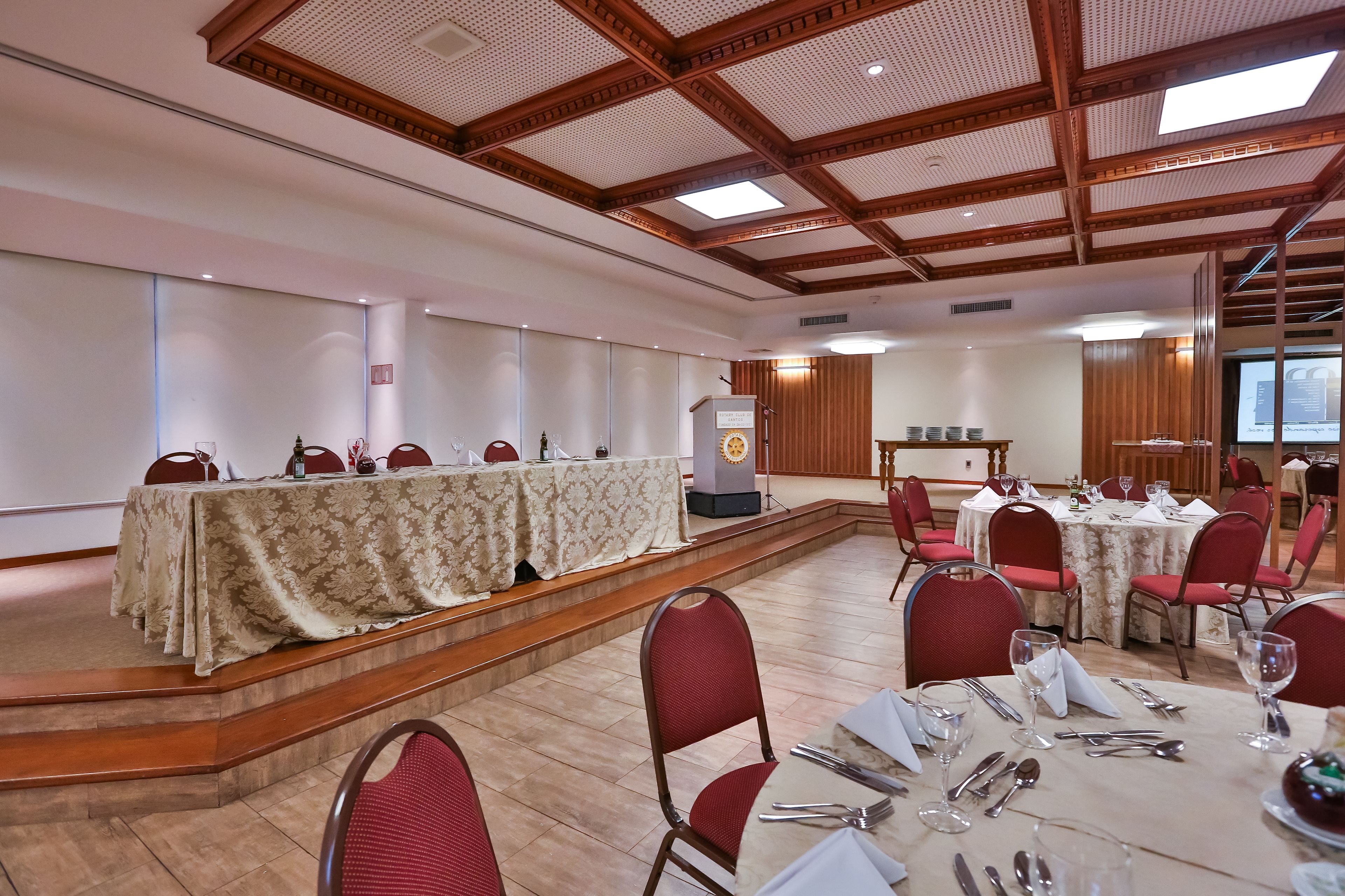 A conference room with a stage, red chairs, and tables set for dining.
