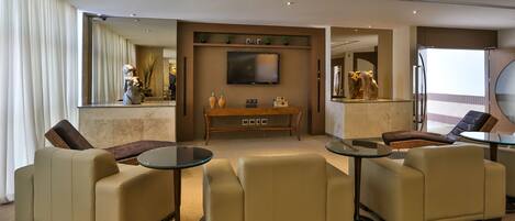A modern hotel lobby with a seating area, a flat-screen TV, and a dining table.