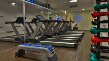 Un gimnasio con cintas de correr, una plataforma elevada y un estante con mancuernas.