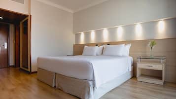 Quarto de hotel moderno com uma cama grande, uma mesa de cabeceira com um vaso e piso de madeira.