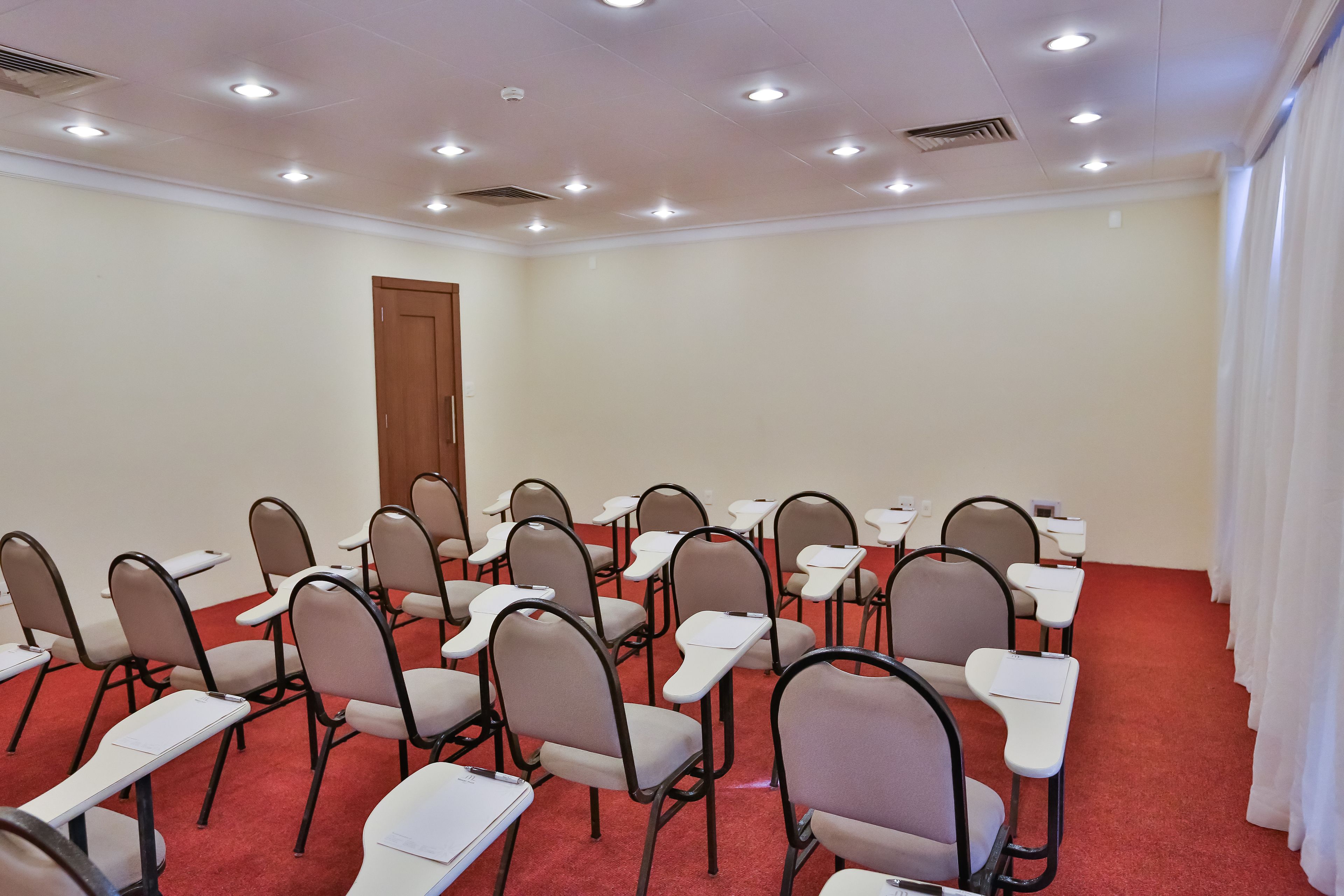 Une salle de conférence avec des rangées de chaises et de tables, une porte en bois et un tapis rouge.