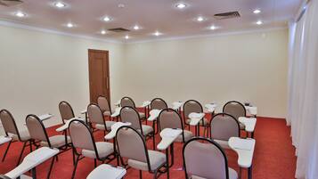 Une salle de conférence avec des rangées de chaises et de tables, une porte en bois et un tapis rouge.
