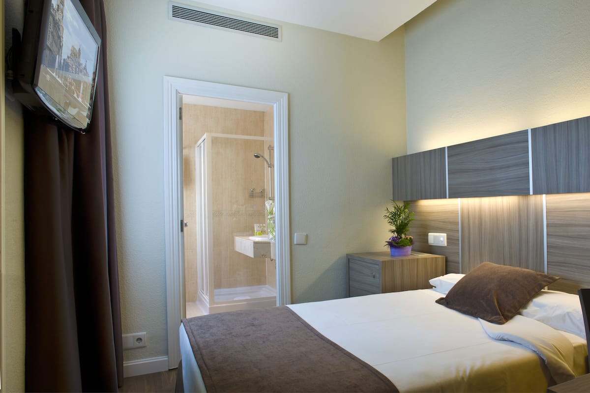 A hotel room with a bed, bedside table, lamp, and a view of the bathroom.