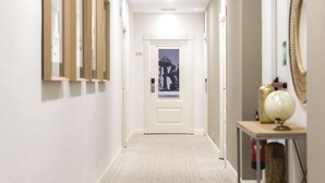 A hallway with a patterned carpet, framed pictures on the wall, a door at the end, and a small table with a globe and vase.