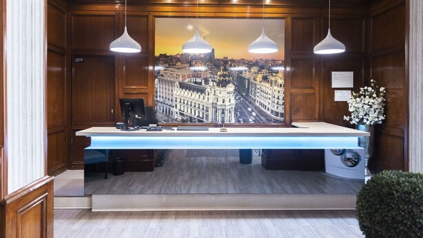 A reception desk with a cityscape view, pendant lighting, and a potted plant.