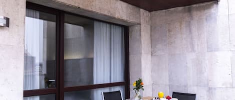 Un balcón con una mesa dispuesta para el desayuno, que incluye un florero con flores, una taza y un plato.