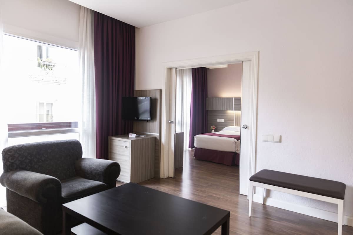 A hotel room with a bed, a desk, a TV, a chair, and a bench.