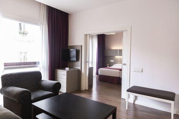 A hotel room with a bed, a desk, a TV, a chair, and a bench.