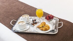 A neatly made bed with a tray of breakfast items including croissants, strawberries, and orange juice.