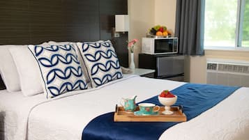 A neatly made bed with a tray of breakfast items, a microwave, and a fruit basket on a small table beside the bed.