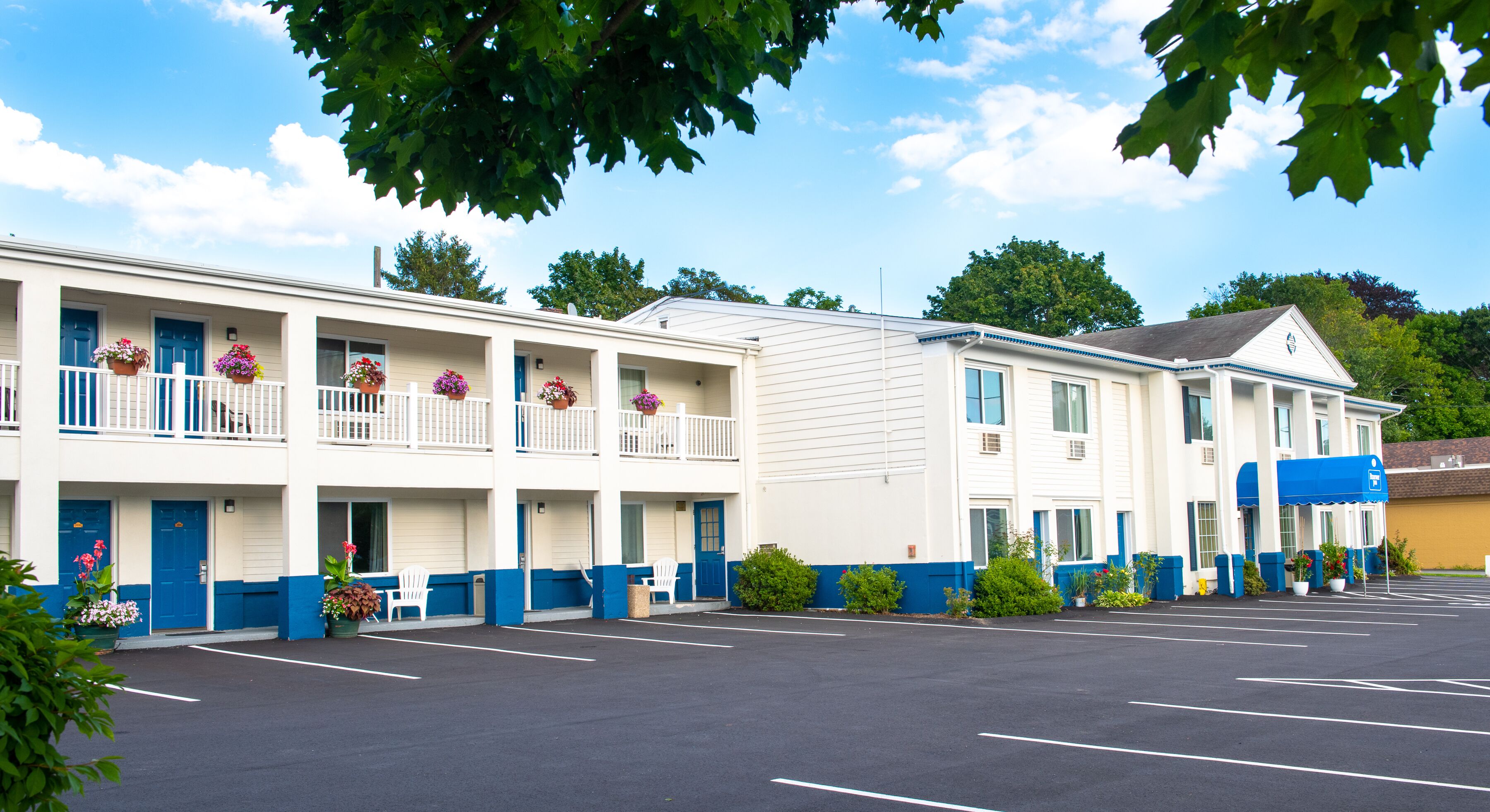 A motel with a parking lot, multiple rooms with balconies, and a blue awning.