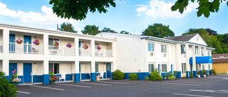 A motel with a parking lot, multiple rooms with balconies, and a blue awning.