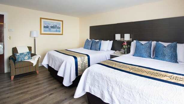 A hotel room with two beds, a wooden floor, a chair, a desk, a lamp, and a framed picture on the wall. - Rodeway Inn Middletown - Newport (Middletown)