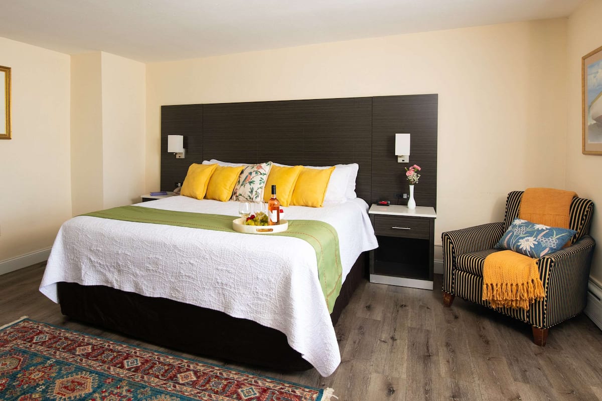 Ein Hotelzimmer mit einem großen Bett, einem Nachttisch, einem Sessel und einem kleinen Tisch mit Blumen.