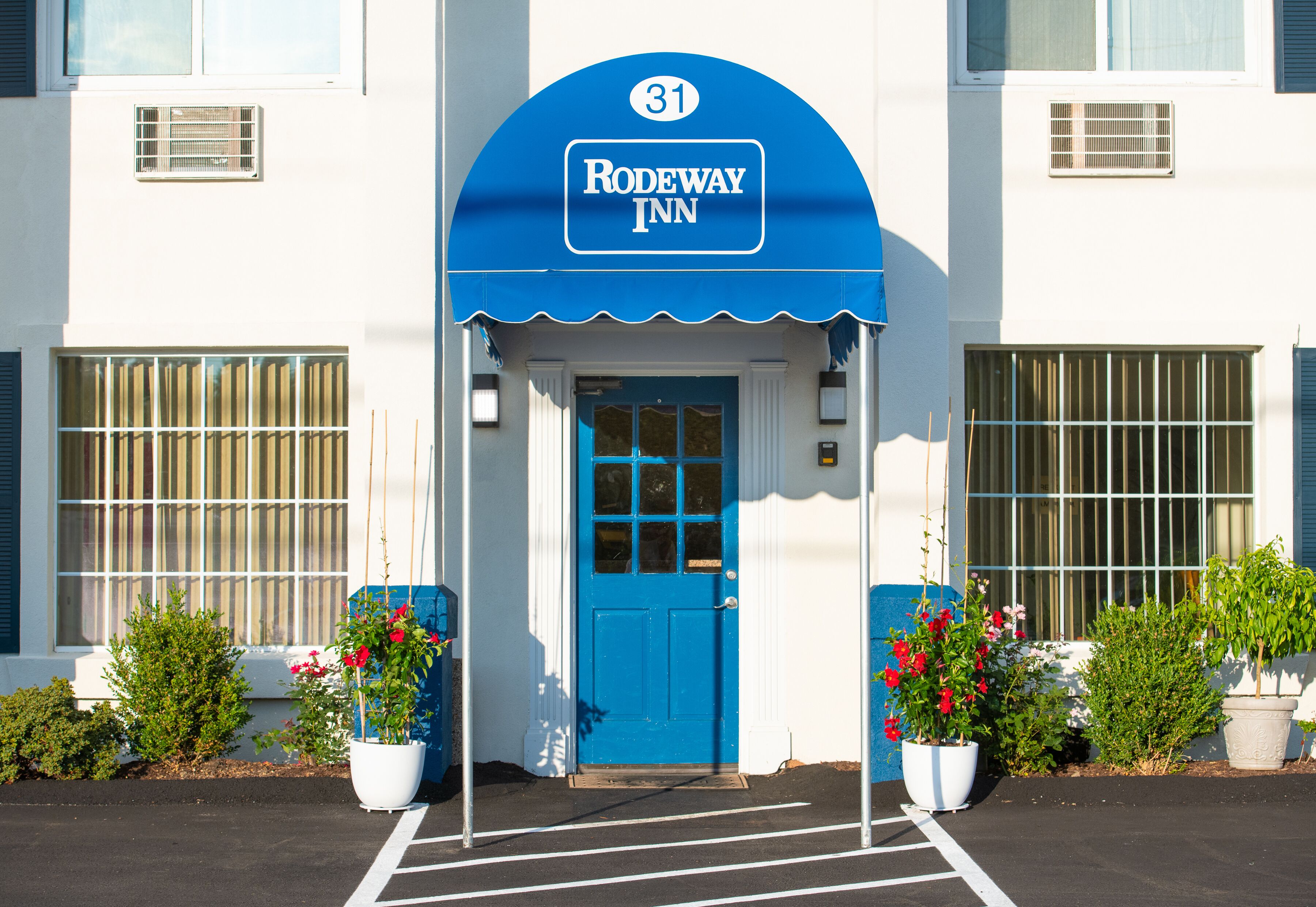 The exterior of a hotel with a blue awning, a number 31 sign, and potted plants.