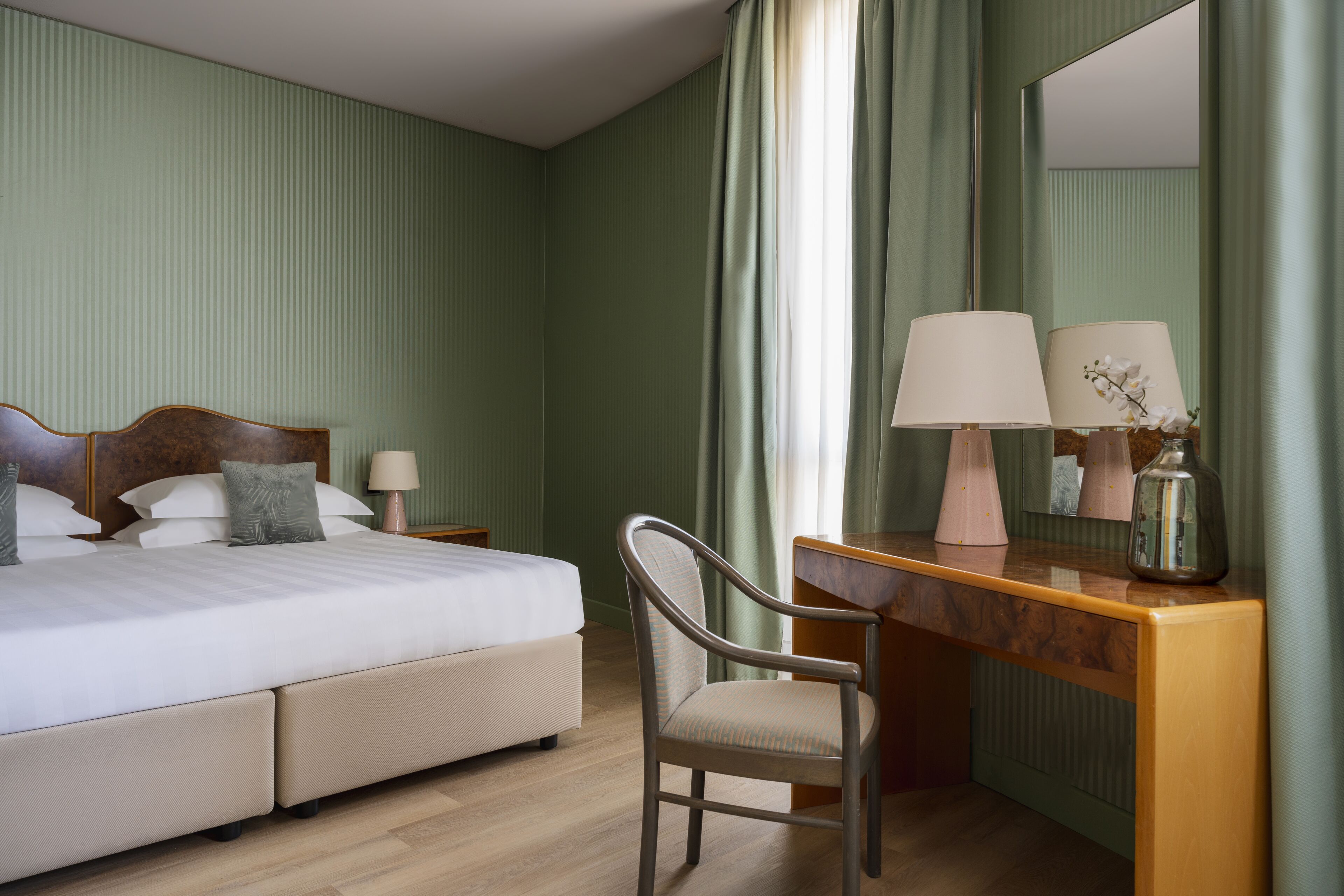 Ein Hotelzimmer mit einem Bett, einem Schreibtisch, einem Stuhl, einem Spiegel und einem Nachttisch mit Lampen.
