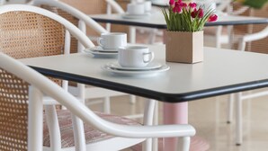 A dining area with white chairs, a table with a vase of pink flowers, and framed artwork on the wall. - Perugia Park Hotel (Perugia)