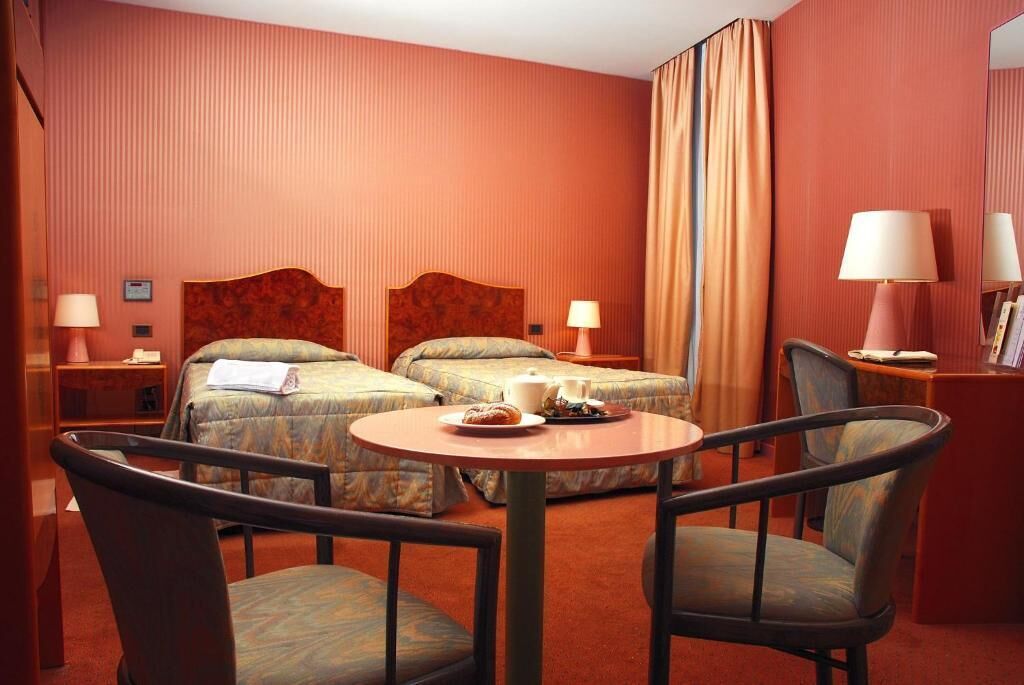 Habitación de hotel con dos camas, una mesa redonda y dos sillas.