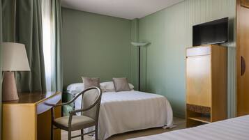 A hotel room with a bed, a desk with a lamp, a chair, a wardrobe, and a television on the wall.