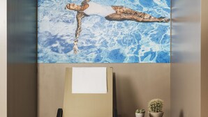 A room with a large painting of a swimming pool, a chair, and a small table with a cactus. - Perugia Park Hotel (Perugia)