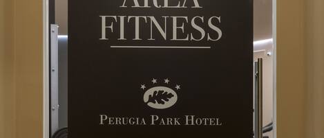A gym area with exercise equipment and a sign that reads "AREA FITNESS Perugia Park Hotel".