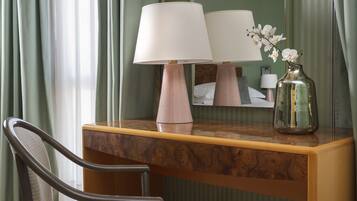 A hotel room with a wooden desk, two lamps, a chair, a mirror, and a vase with flowers.