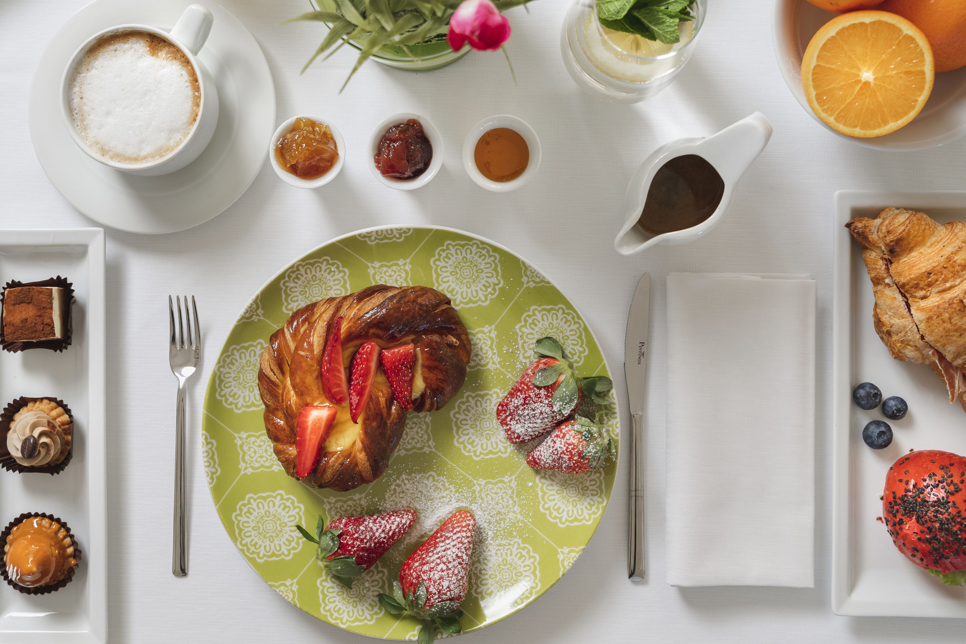 A breakfast setting with a croissant, strawberries, and a cup of coffee on a white table.
