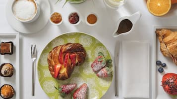 Desayuno con un croissant, fresas y una taza de café sobre una mesa blanca.
