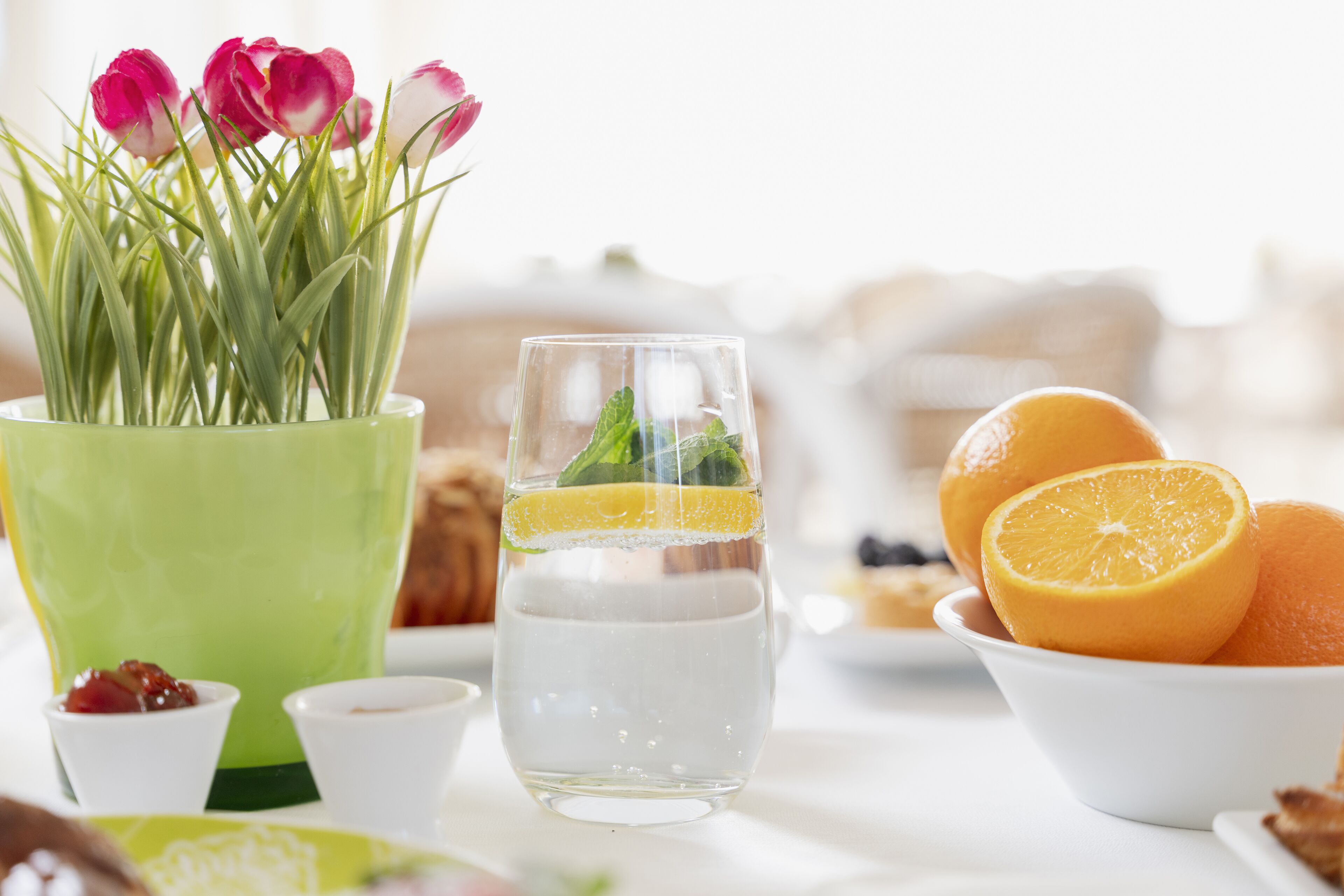 Un tavolo con un bicchiere d'acqua, una ciotola di arance e un vaso di tulipani.