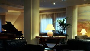 A modern living room with a glass coffee table, black leather sofas, a piano, and a painting on the wall. - Perugia Park Hotel (Perugia)