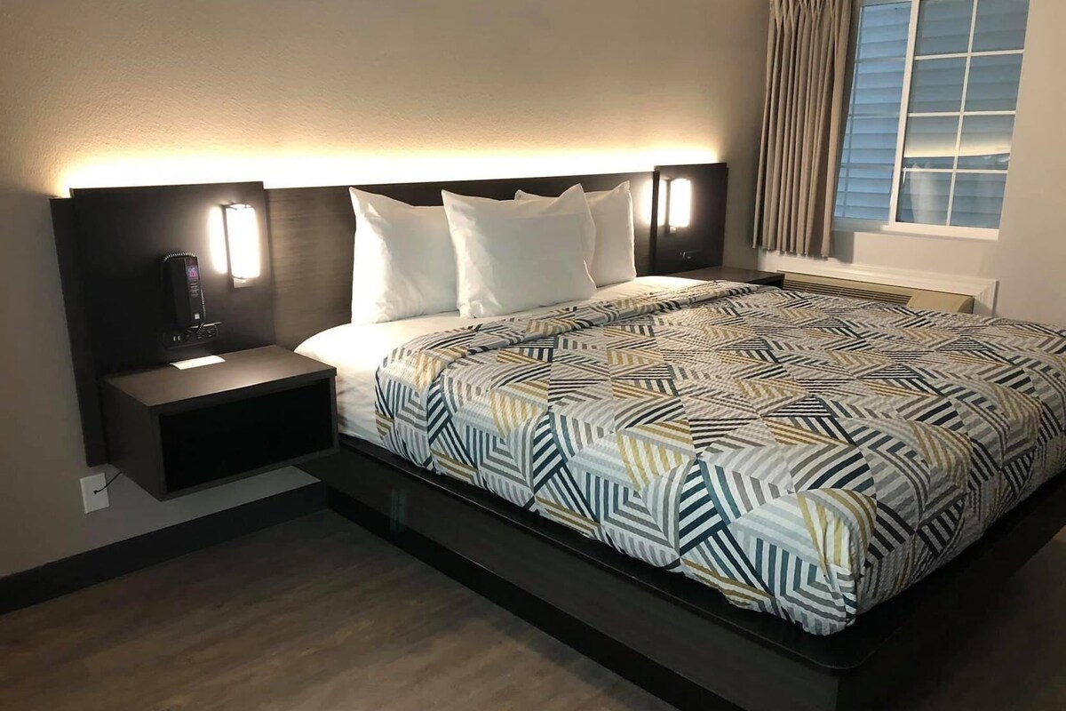 A modern hotel room with a bed, bedside tables, and a nightstand.