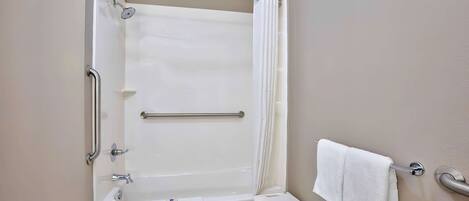 A bathroom with a bathtub, a shower, a grab bar, a towel rack, and a small step stool.